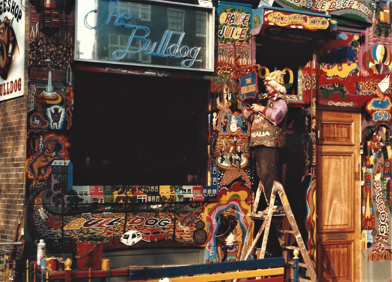 Artist Harold “Kangaroo” Thornton standing on a ladder, painting the psychedelic exterior of The Bulldog coffeeshop in Amsterdam.